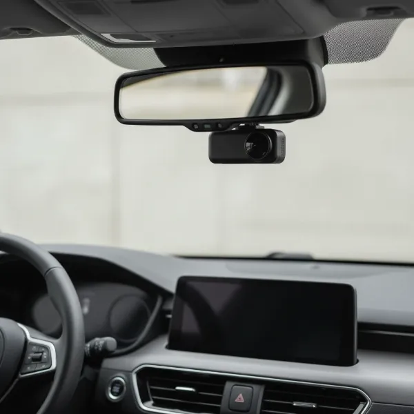 A discreet dash cam mounted behind a car's rearview mirror, blending into the interior to prevent theft