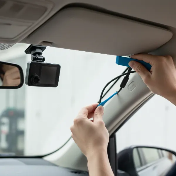 A person carefully tucking a dash cam power cable along the car's A-pillar.